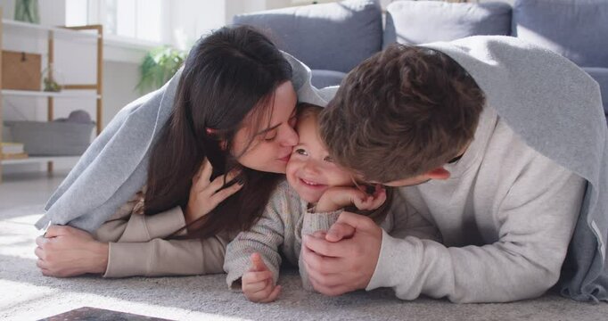 Happy family, mother, father and young daughter close under blanket on loving hug, happy emotion, parents, child gentle bonding, enjoy good time together, healthy understanding relationships, playing