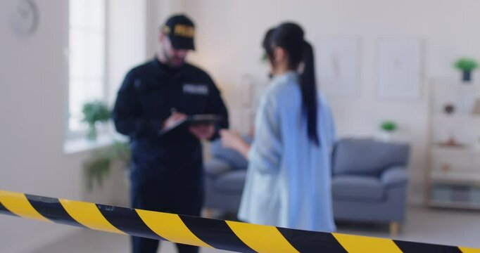 Portrait of a young police man officer talking to witnesses making interview or interrogating young worried woman robbery victim after burglary at home standing at crime fenced scene. 4k video.
