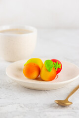 Candies from marzipan in the form of fruits with a cup of coffee on the white table. Vertical orientation.