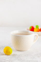 A cup of cappuccino coffee with marzipan candies in the form of lemon on the table. Vertical orientation.