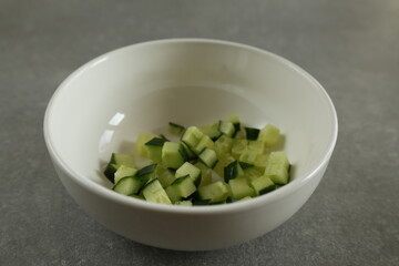 Diced green fresh cucumber in a white bowl.