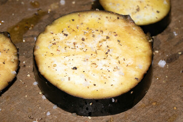 A seasoned sliced aubergine eggplant with salt and herbs waiting to be cooked in the oven close up raw