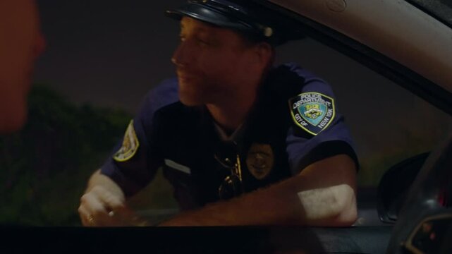 Police officer leans on a car window at night, discreetly accepting a bribe from the driver. Officer takes the money and allows the driver to leave. Police corruption, no trust in law enforcement.