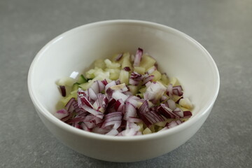 A white bowl filled with a mix of diced red onion, cucumber, and Hungarian wax pepper.