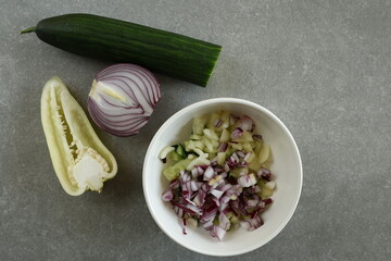 A white bowl filled with a mix of diced red onion, cucumber, and Hungarian wax pepper.
