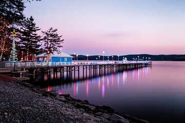 Fototapeta premium Scenic pier decorated with colorful holiday lights at dusk, reflecting on calm waters.