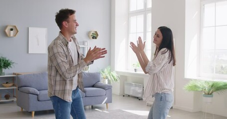 Happy young couple giving high five and dancing at home in living room celebrating moving into new apartment or enjoying a good mood and happy life moments together. 4k video. Slow motion video.