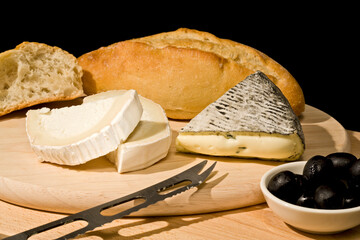 blue mold cheese and goat cheese with white bread and black olives on wooden platter