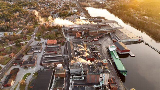 Industrial peper mill complex plant emitting smoke on the river bank at sunset