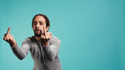 Irked man fighting with friend, doing middle finger sign gesturing, isolated over studio...