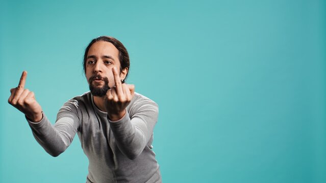 Irked man fighting with friend, doing middle finger sign gesturing, isolated over studio background. Outraged person arguing during conversation, doing obscene hand gestures, camera B