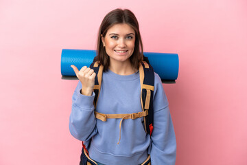 Young mountaineer woman with a big backpack isolated on pink background pointing to the side to present a product