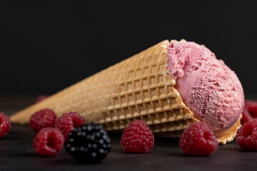 red raspberry ice cream in a waffle cone on a black background