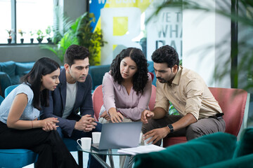 Marketing Team Sitting At Meeting Table Looking At Laptop Screen And Talking