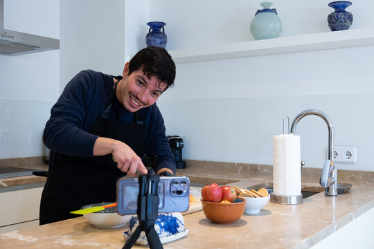 Cheerful young man cutting with a knife some apples making a tutorial of a recipe of a dessert with apples and cookies at home