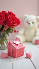 Pink polka dot gift box tied with ribbon, two pink heart decorations a bouquet of red roses with a lovely white teddy bear in the background, love concept.
