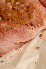 a salted piece of fresh chicken meat on paper sprinkled with spices