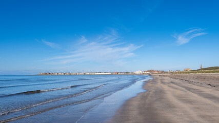 Looking over the waters of Troon Bay Bay in Scotland with blue Skys and gentle waters lapping the beach.