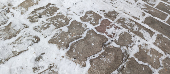 Snow on the paving slabs. An unpeeled sidewalk. Winter road cleaning.