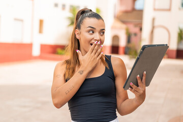 Young pretty woman holding a tablet at outdoors with surprise and shocked facial expression