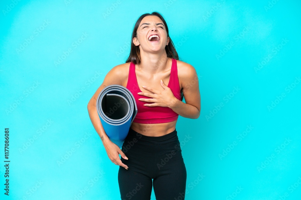 Poster Young sport caucasian woman going to yoga classes while holding a mat isolated on blue background smiling a lot