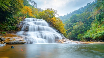 The Tropical waterfall in the forest and mountain of Khao Lak in South Thailand cascades down a lush green cliff, surrounded by vibrant tropical foliage and shimmering pools of crystal clear water