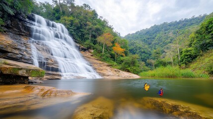 The Tropical waterfall in the forest and mountain of Khao Lak in South Thailand cascades down a lush green cliff, surrounded by vibrant tropical foliage and shimmering pools of crystal clear water