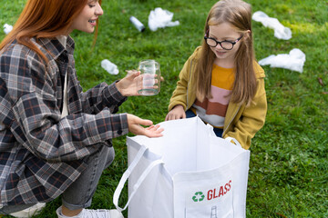 Fototapeta premium Teacher guiding child in collecting glass waste in park to reduce pollution