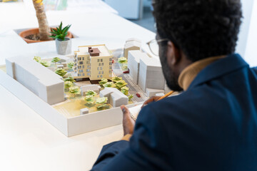 African american young architect sitting at the table and analyzing new model