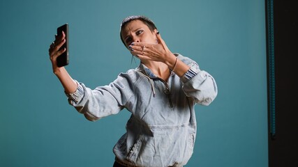 Silly confident woman recording a video while she shows groovy dance moves, filming on her smartphone and fooling around in studio. Funky bold edgy person being funny. Camera A.