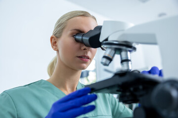 Fototapeta premium Woman technician in lab looking at samples under microscope for test in pharmaceutical research