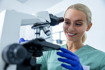 Medical woman in laboratory studying samples under microscope with protective gloves