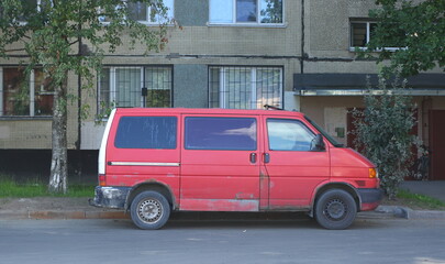An old rusty red minibus is parked in the courtyard of an apartment building, Podvoysky Street, St....