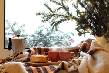 cups bun geyser coffee maker and fir tree with blanket on window background. cozy winter morning