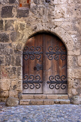 An ancient wooden door with intricate iron details set within a medieval castle's stone wall, exuding historical charm and craftsmanship.