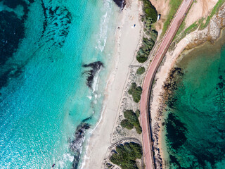 The isthmus connecting Capo Testa to mainland Sardinia, showcasing turquoise waters, sandy beaches, and a scenic coastal road surrounded by natural beauty.