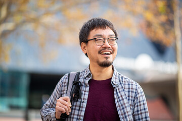 Smiling Asian man with a backpack looking away outdoors