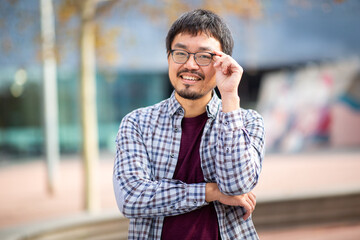 Friendly Asian man adjusting glasses and smiling outdoors