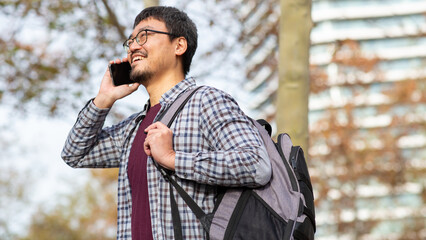 Smiling Asian man talking on phone in outdoor urban park