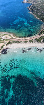 The isthmus connecting Capo Testa to mainland Sardinia, featuring turquoise waters, sandy beaches, and a coastal road surrounded by lush greenery and rocky shores.