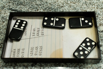 A few dominoes in the top of the domino box with the score card. 