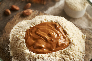 Whey protein powder, ground oat flakes and nut butter in a glass bowl - ingredients for homemade protein chocolate bars