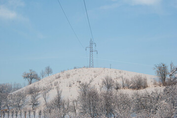 Snowy winter landscape with an electric tower on a hill.