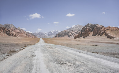 Asphalt road of the Pamir Highway in the valley of the Tien Shan Mountains in Tajikistan in the Pamirs, landscape in the high desert mountains for background, the road goes into the distance