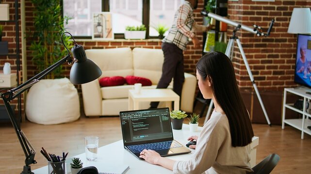 Software developer types programming code in a cozy home office setup. Asian woman coding for cloud computing on her laptop, enhances productivity for software development. Camera A.