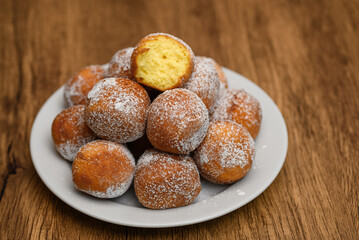 Małe pączki na talerzu obsypany cukrem oudrem, jeden nadgryziony