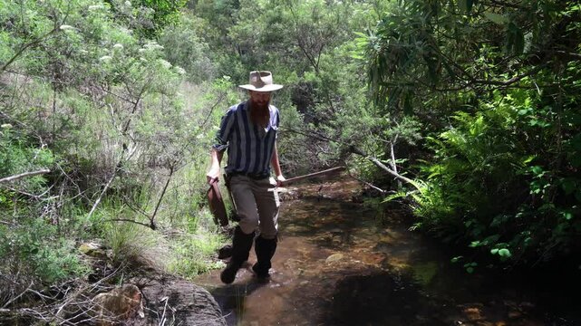 Traditional Australian gold prospector exploring through a forest creek with a pan in his hand.