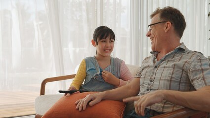 Obraz premium Grandfather and granddaughter together watch interesting entertainment media on TV. Old senior use technology communicate with young generation cross generation gap strengthen family bond. Divergence.
