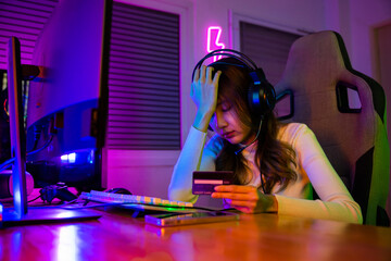 Young Asian woman gamer wearing headphones unset suffer of overspending money from card account...