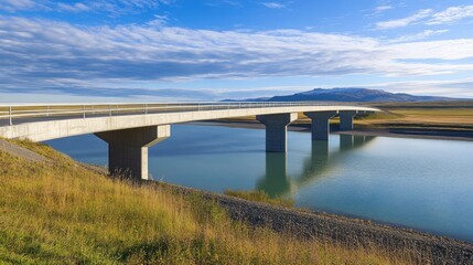 Fototapeta premium A modern bridge spans a tranquil river under a blue sky, surrounded by lush landscapes.